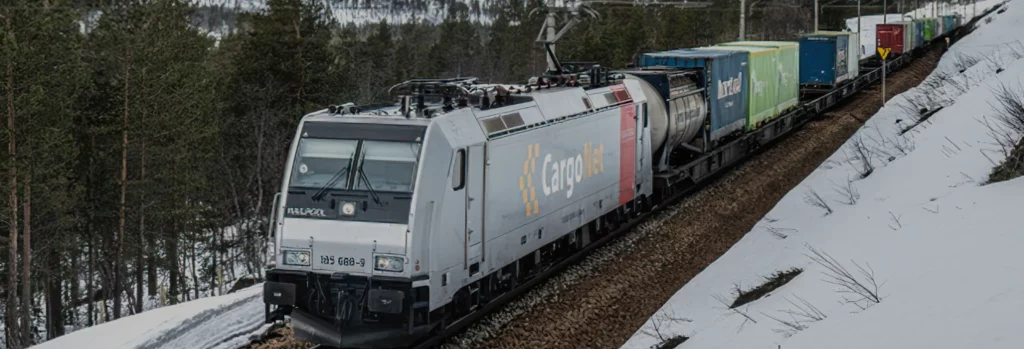 Langt godstog med forskjellige fargerike fraktcontainere kjører ned snødekte jernbanespor